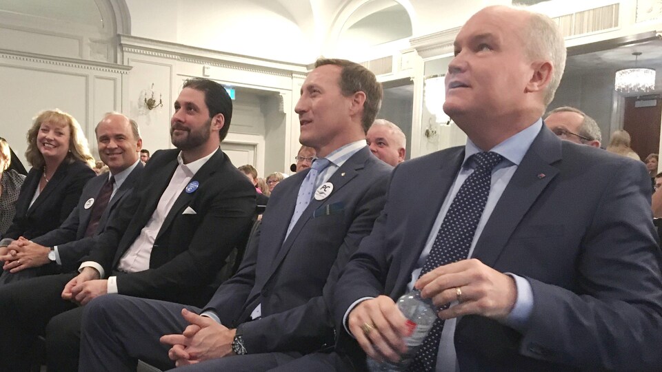 Cinq candidats à la direction du Parti conservateur du Canada sont assis en rang sur des chaises.