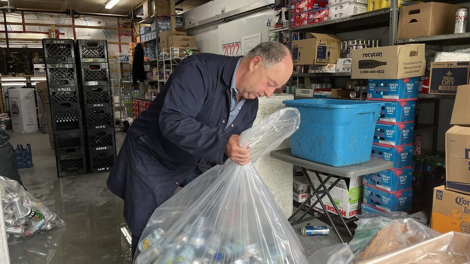 Réal Thériault met des canettes dans des sacs en plastique, il se trouve à l'intérieur d'un entrepôt.