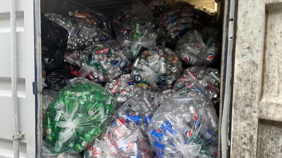 Des dizaines de sacs remplis de canettes et de bouteilles de plastique vides se trouvent dans un conteneur.