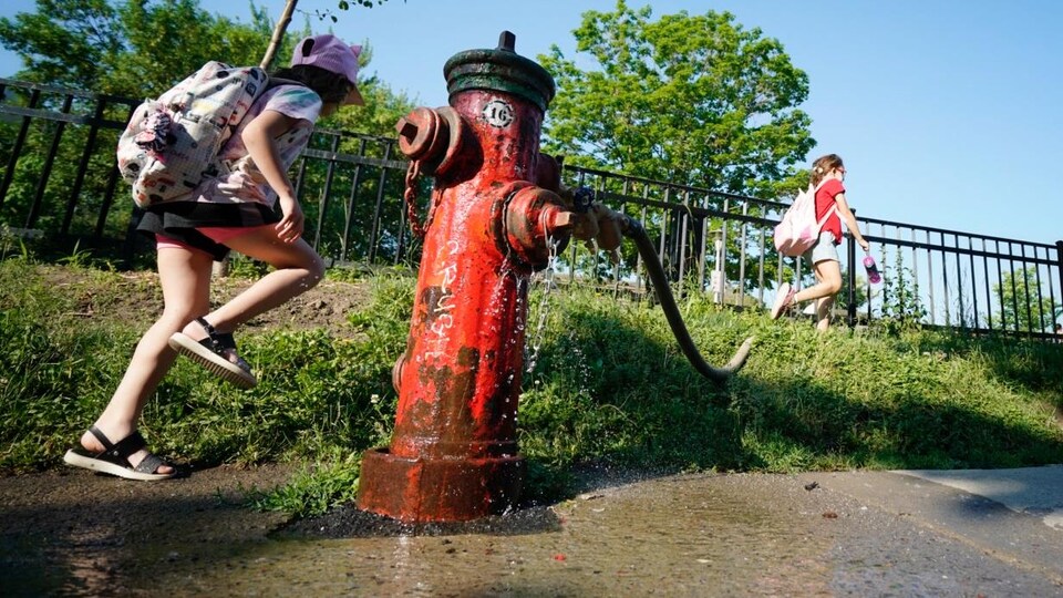 Des enfants marchent près d'une borne-fontaine de laquelle s'écoule de l'eau.                              