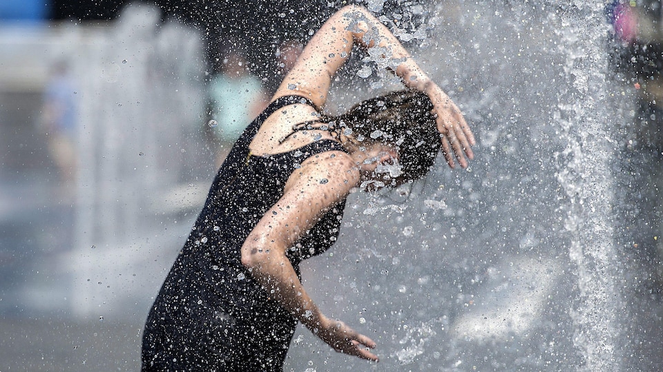 Une femme se rafraîchit dans une fontaine, à Montréal, pendant la canicule. 