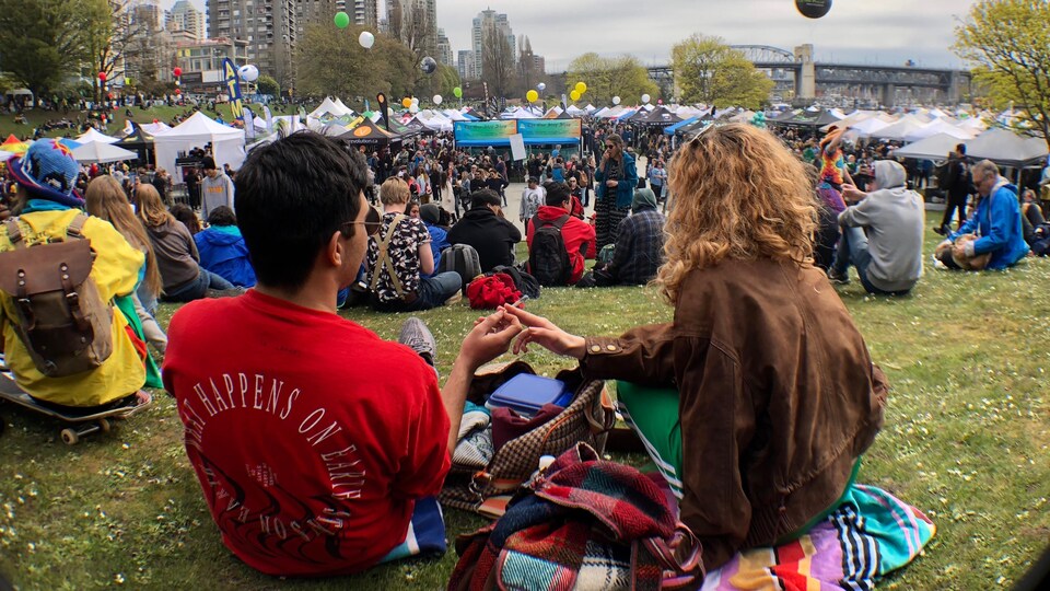 En avant-plan un homme et une femme s'échangent une cigarette de cannabis et en arrière-plan une foule et des tentes. 