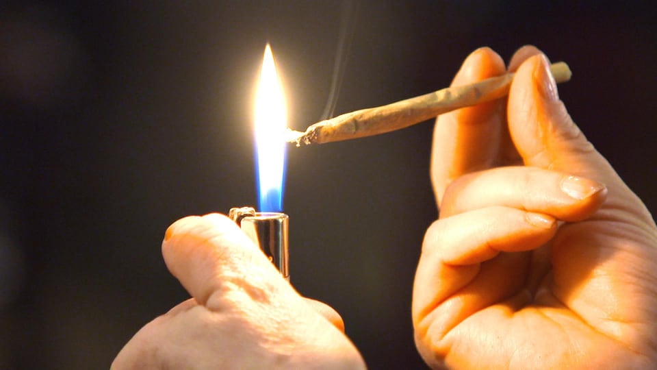 Une personne s’allume un joint de marijuana.