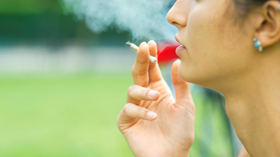 Une femme fume une cigarette de marijuana.