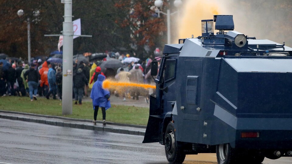 Un canon à eau arrosant un manifestant de dos. 