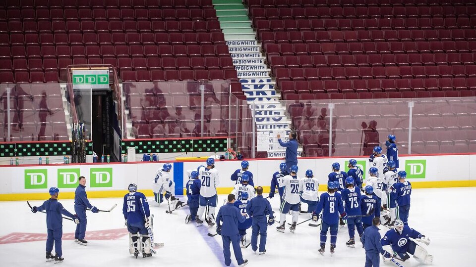 Les joueurs entourent leur entraîneur-chef Travis Green sur la patinoire.