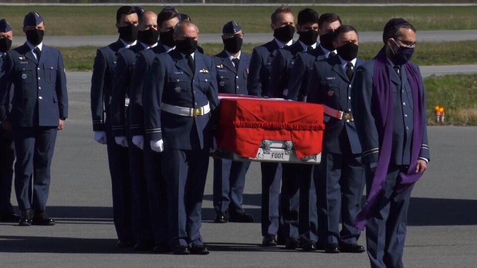 Plusieurs hommes masqués portent un cercueil. 
