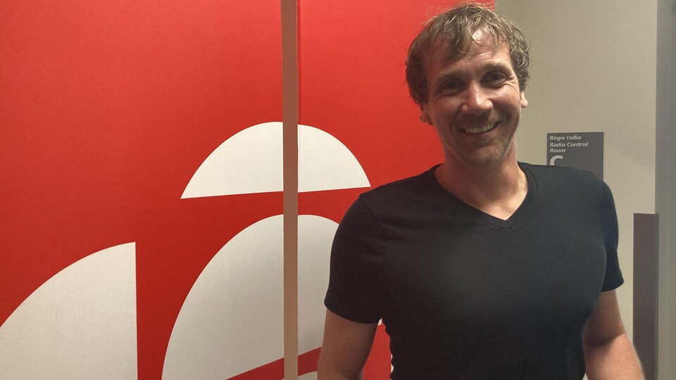 Yannick Gagnon pose devant une affiche de Radio-Canada.