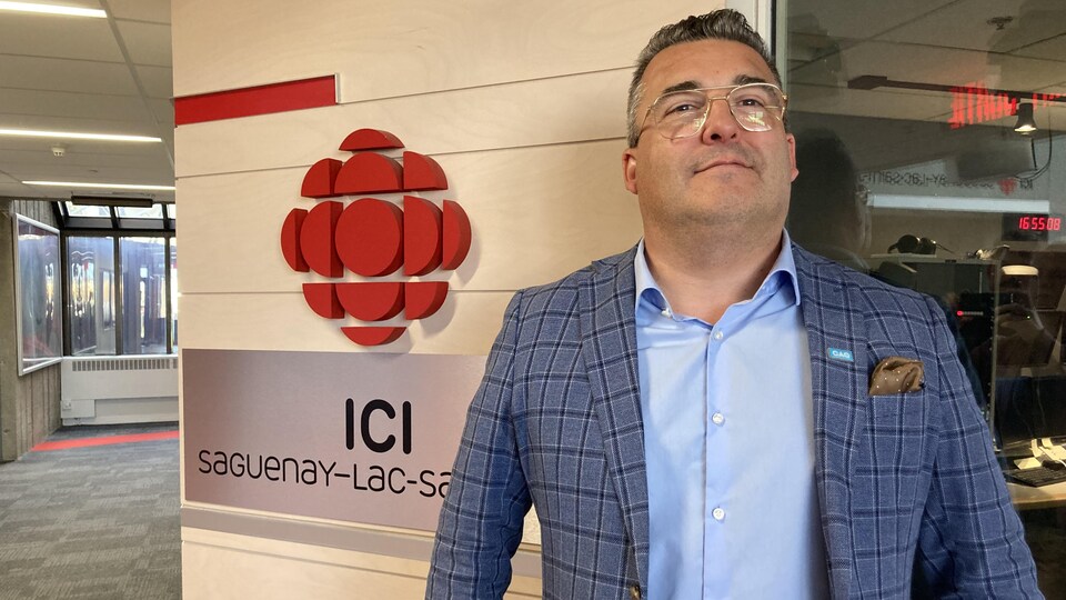 Un homme pose devant un mur avec un logo de Radio-Canada.