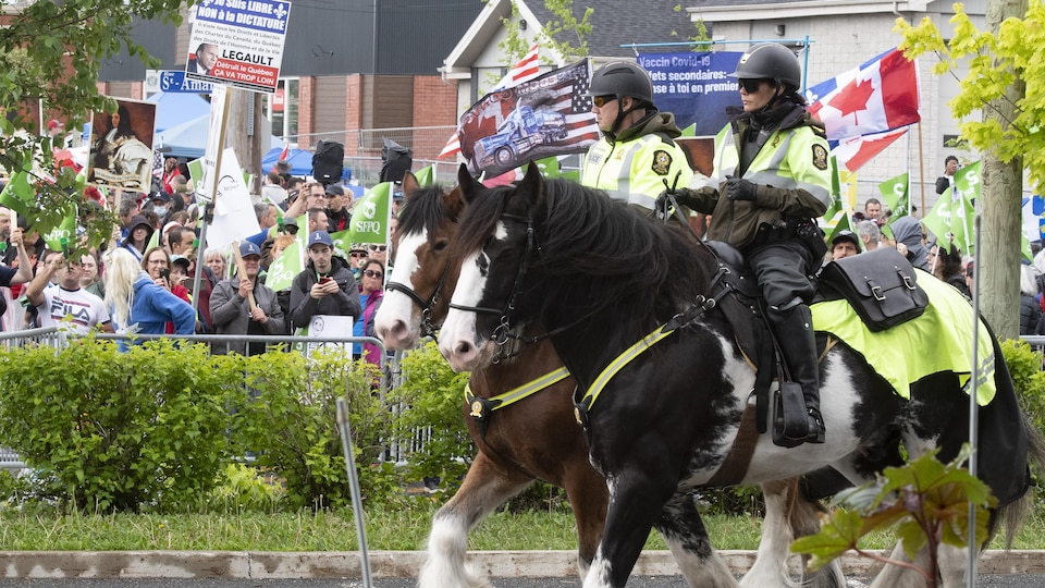 Deux policiers à cheval patrouillent à proximité de manifestants.