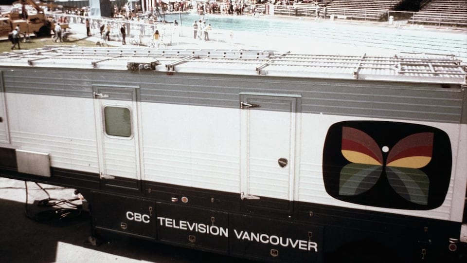 À l'extérieur, une unité mobile de télévision de Radio-Canada à Vancouver est stationnée près d'un site de compétition sportive de natation.