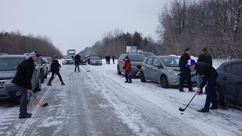 Des gens jouent au hockey entre des voitures stationnées, sur l'A-40.