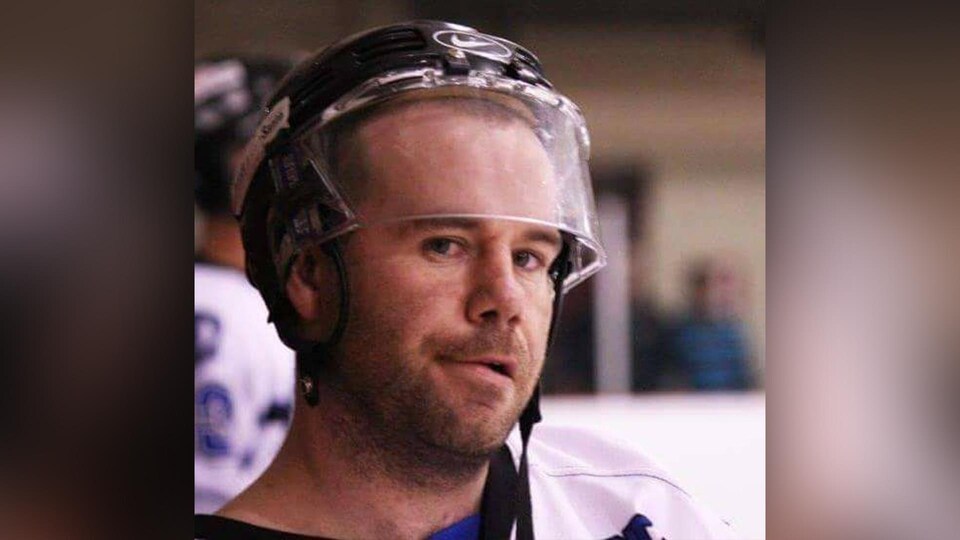 L'homme est à l'aréna et porte un casque de hockey.