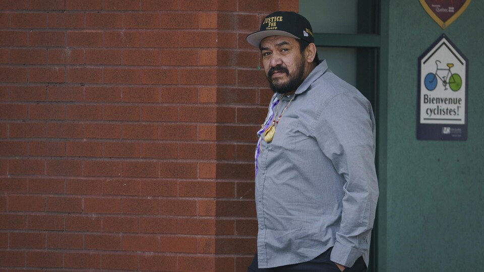 Un homme portant une casquette sur laquelle est écrit « Justice for Joyce » marche le long d'un mur.