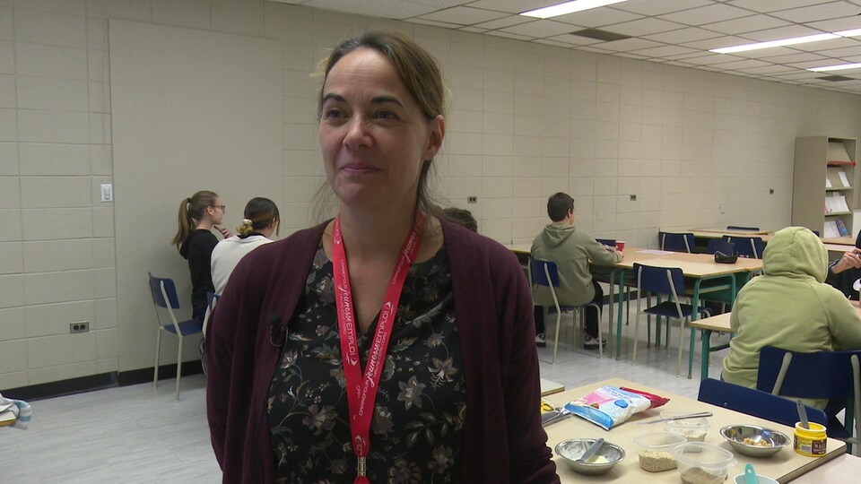 Caroline Jean est dans la classe entourée d'élèves qui cuisinent. Des aliments se trouvent derrière elle.