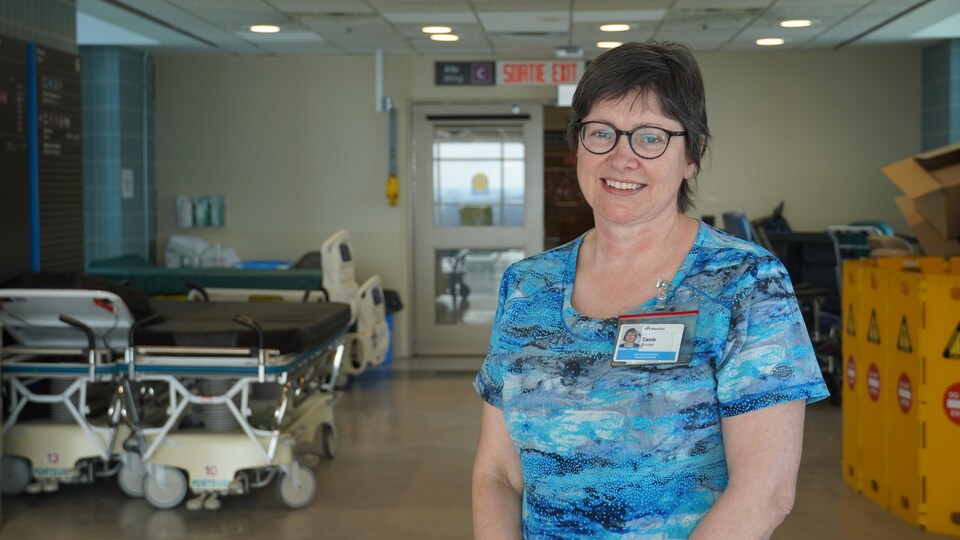 Une infirmière pose dans un couloir d'hôpital devant des civières, pour une photo.