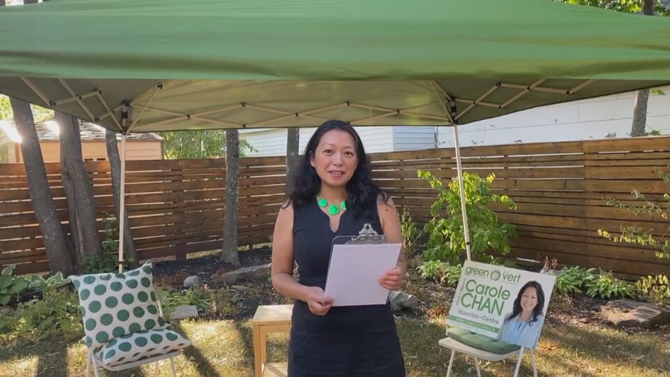 La candidate à la chefferie, Carole Chan, se tient debout à côté de sa pancarte électorale.