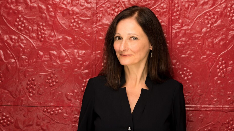 Carole Freynet-Gagné pose devant un mur rouge avec des reliefs de raisins et de vignes.