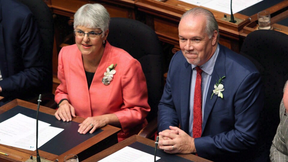 Une femme à gauche à côté d'un homme à droite.assis à l'intérieur d'une chambre législative.