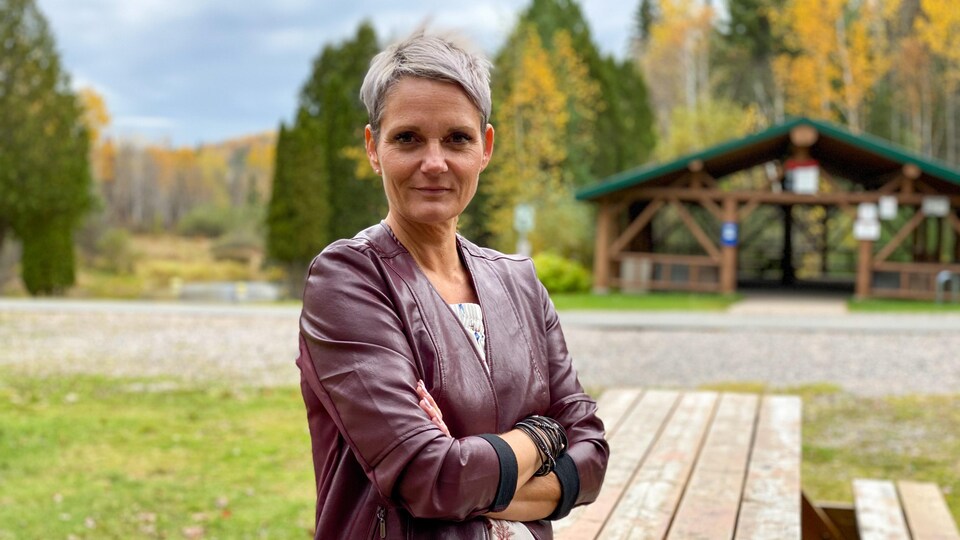 Une femme aux cheveux courts gris croise les bras devant l'objectif.
