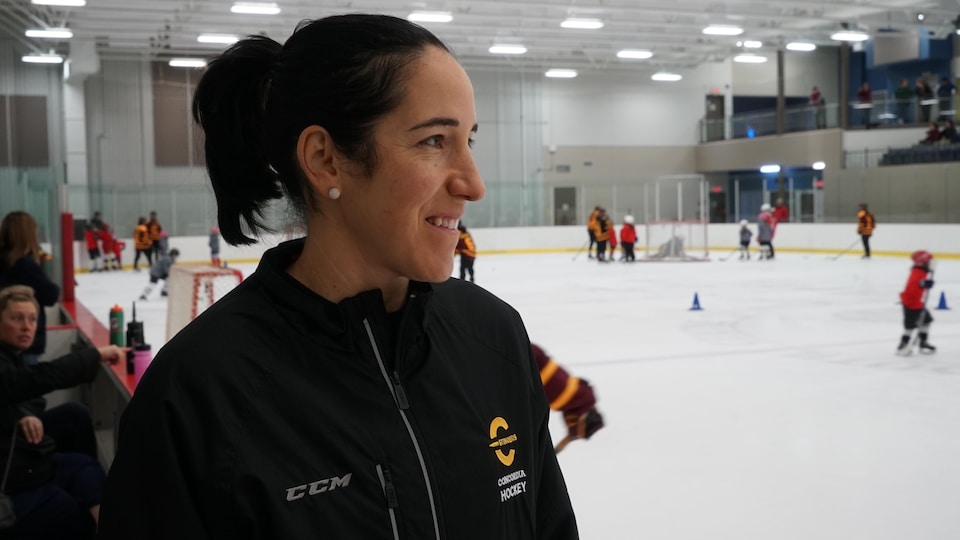 Une femme habillée en noir se tient debout tout près d'une patinoire intérieure.