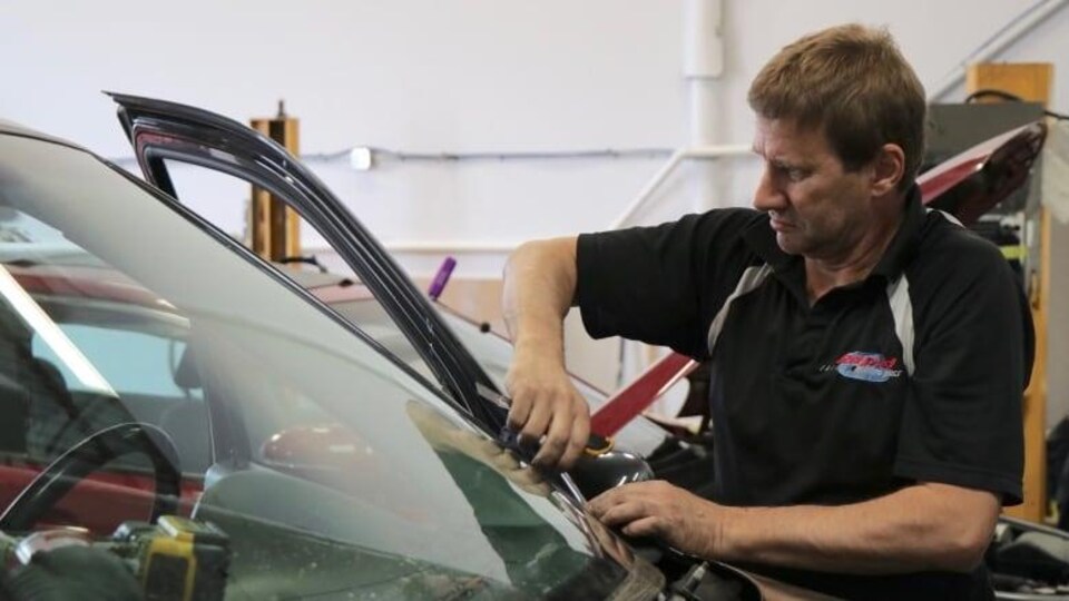 Un homme installe un pare-brise sur une auto.