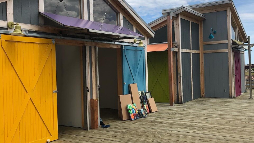 Des cabanes sur un quai avec des toiles déposés contre un mur.
