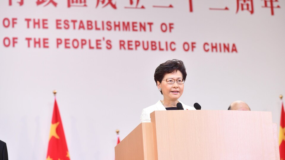 Une femme asiatique parle au micro devant un mur sur lequel il est écrit, en anglais et en langue chinoise, « La république populaire de Chine ».