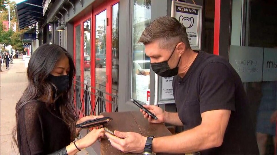 Une femme présente son téléphone cellulaire à un homme devant la porte d'un commerce.