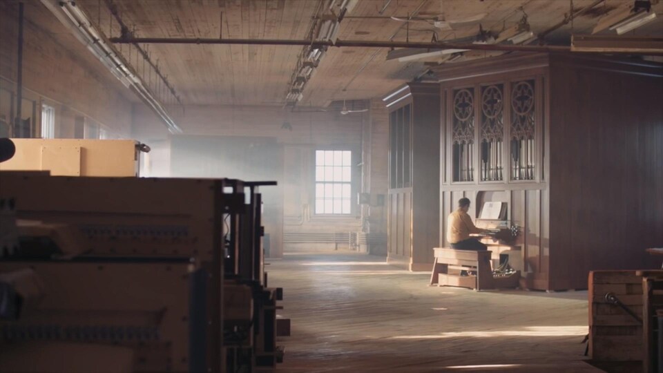 Un homme est assis à un orgue au fond des ateliers de Casavant Frères.