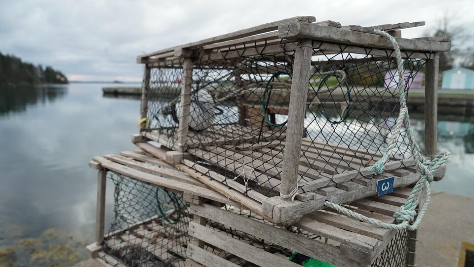 Trois casiers à homard en bois empilés sur un quai, au bord de l'eau.