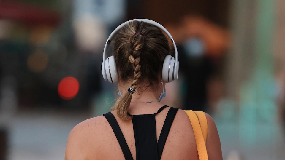 Une femme de dos se promène dans la rue avec un casque d'écoute sur la tête. 