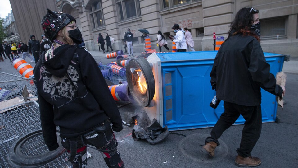Deux manifestantes se tiennent près d'une toilette portative en feu.