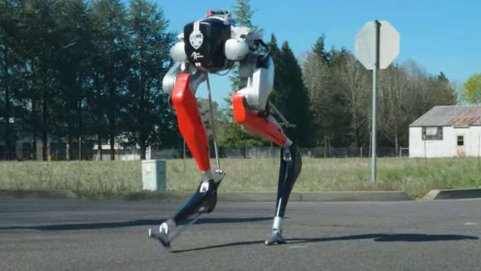 Un robot bipède court sur un chemin asphalté.