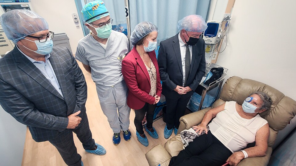 Quatre personnes regardent une patiente couchée avec un bandage à l'oeil. 