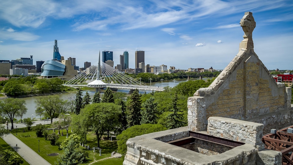 Une vue aérienne depuis les murs de pierre de l'ancienne cathédrale de Saint-Boniface, où l'on voit l'esplanade Louis-Riel, le pont Provencher, le Musée canadien pour les droits de la personne et des immeubles de Winnipeg.