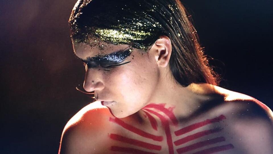 Une Atikamekw est peinte de symboles tribaux et a des paillettes dorées dans ses cheveux.
