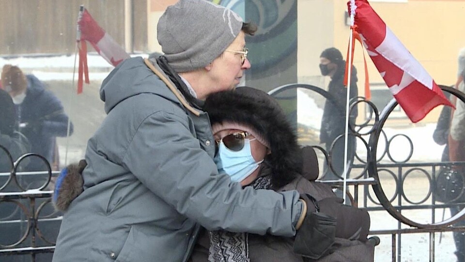 Une femme réconforte une autre femme masquée, à l'extérieur à Ottawa.