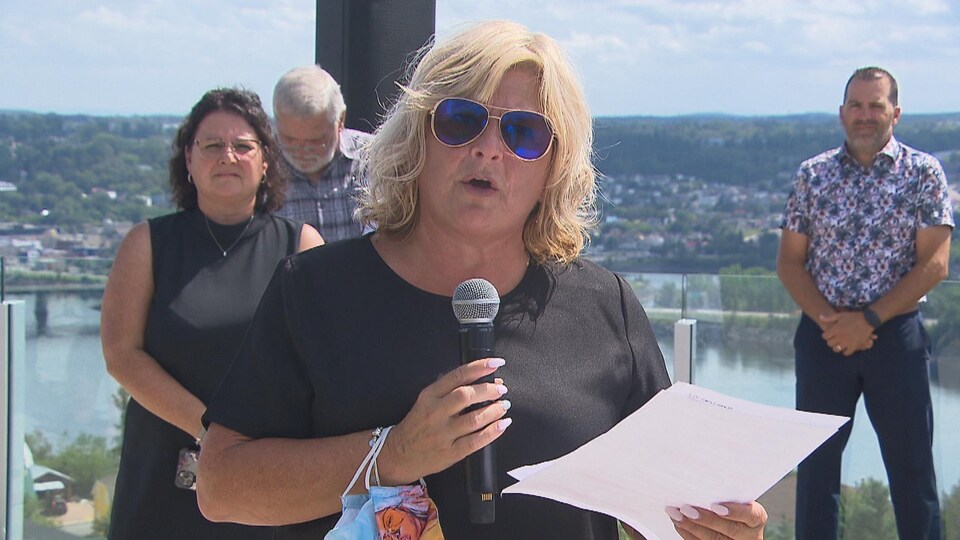 Catherine Morissette tient un micro et parle aux médias, accompagnée de membres de son équipe.