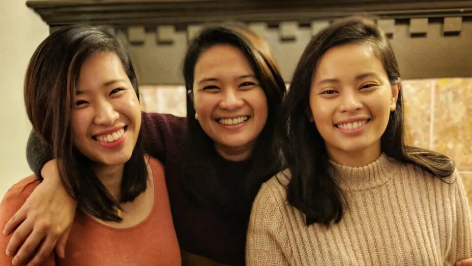 Anne Ignacio (au centre) pose avec ses deux soeurs devant un foyer.