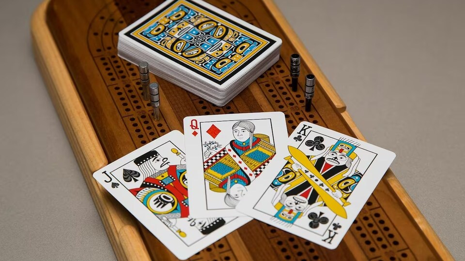 Trois cartes à jouer et une pile de cartes sont déposées sur une planche de cribbage.