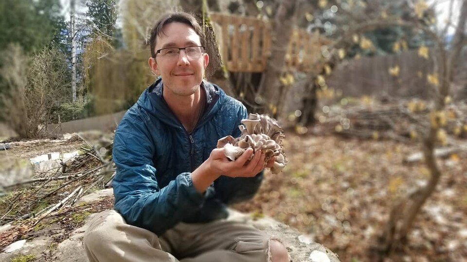 Un homme assis dans un bois tient des champignons.