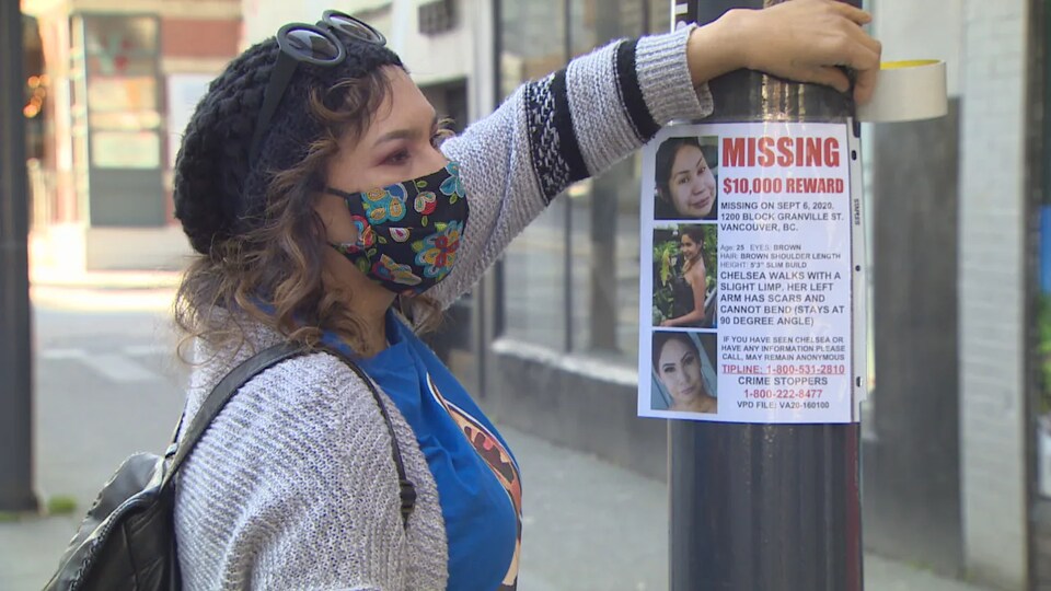 Sheila Poorman colle un avis de recherche protégé par une enveloppe de plastique transparente sur un poteau de la rue Granville, au centre-ville de Vancouver.