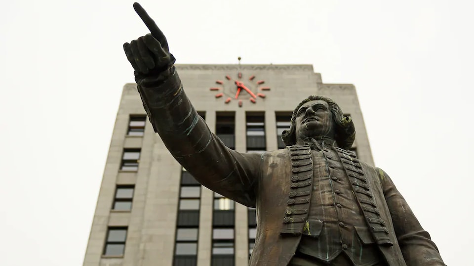 Une statue de George Vancouver pointant au loin trône devant l'Hôtel de Ville de Vancouver et son horloge iconique, en Colombie-Britannique.