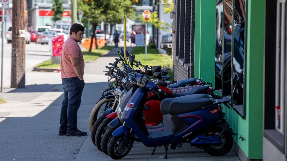 Un homme observe des scooters électriques devant la boutique de Motorino Electric, à Vancouver.