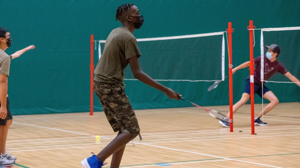 Des adolescents qui portent un masque jouent au badminton dans un gymnase.