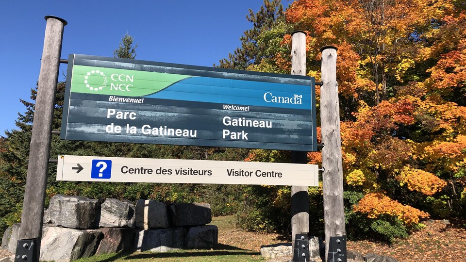 Affiche de la CCN à une des entrées du parc. Derrière, des arbres aux feuilles jaunes et orange.
