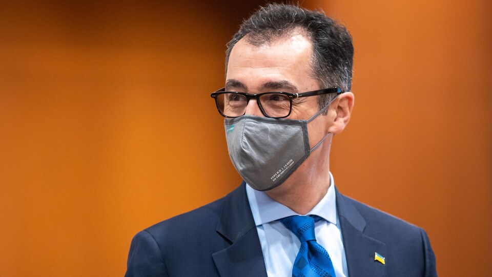 Photo of Cem Özdemir wearing a mask in front of an orange background.