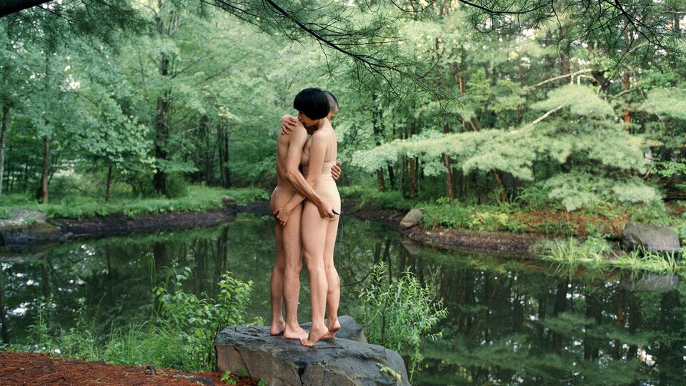 un homme et une femme nue s'enlacent, au bord d'un étang.
