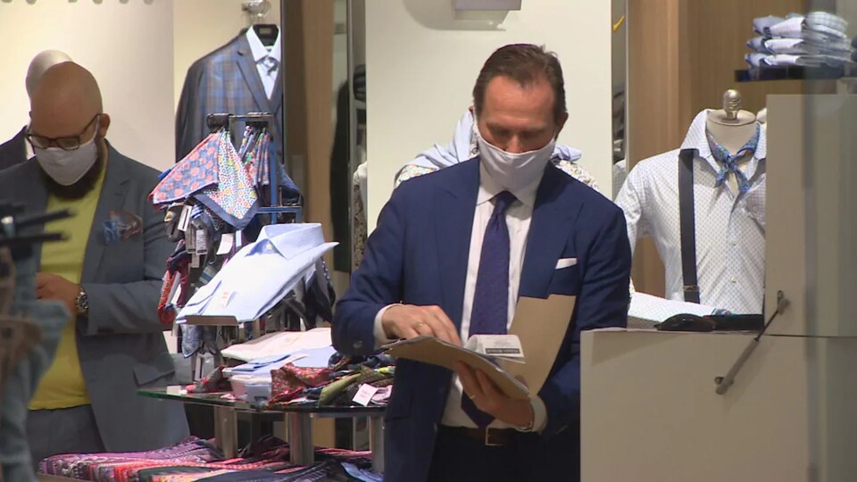 Deux vendeurs dans un magasin de vêtements pour homme . Ils portent chacun un masque pour couvrir leur bouche et leur nez.